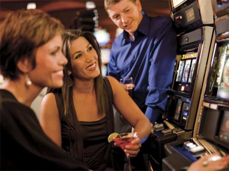 A girl is sitting at the slot machine, and her friends are watching her playing
